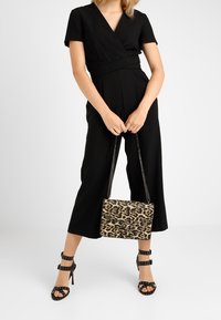 Czarny kombinezon z krótkimi rękawami i kopertowym fasonem, zestawiony z torebką w nadruk lamparta oraz czarnymi sandałami na obcasie z ćwiekami.