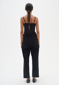 Top aderente nero e jeans neri a vita alta e gamba larga. Tessuto liscio, design minimale. Calzature nere completano il look.