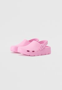Rosa plastklumpar med ett baksnår, med ventilationshål och en tjock, texturerad sula för grepp. Slät yta, rundad tådesign.
