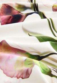 Tissu blanc avec des plis doux, présentant un imprimé floral détaillé en nuances de rose, vert et marron.