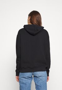 Svart huvtröja med en avslappnad passform, lång ärm och en texturerad fleeceinredning. Kombinerad med blå denimjeans.