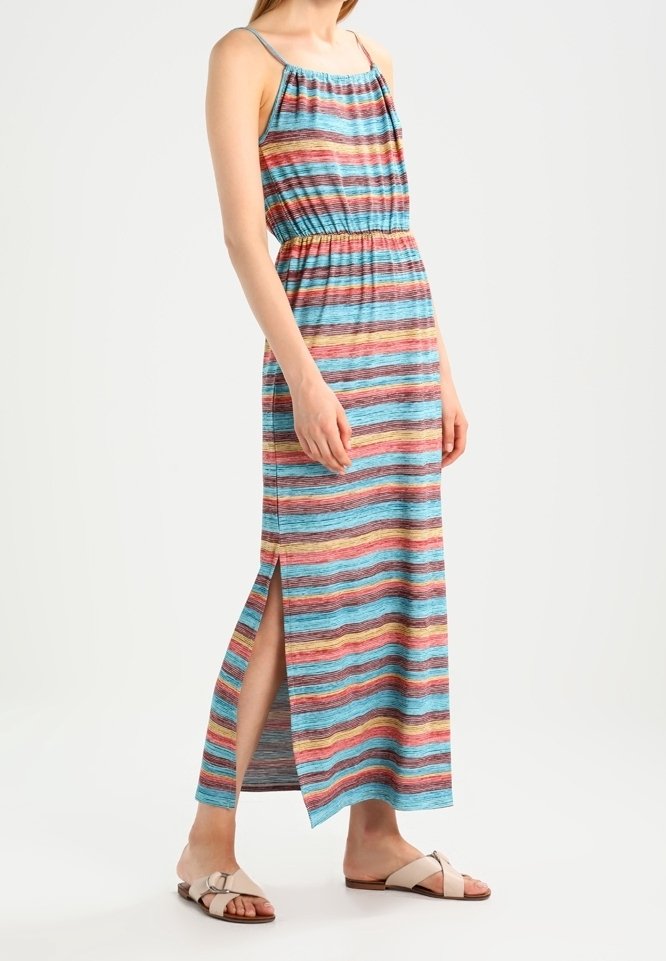 Femme portant une robe sans manches longue jusqu'aux chevilles avec des rayures horizontales multicolores et une fente latérale, associée à des sandales plates beige.