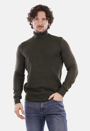Maglione lavorato a maglia di un verde scuro con colletto alto, motivo testurizzato e maniche lunghe, abbinato a jeans in denim blu. Nessun accento notevole visibile.
