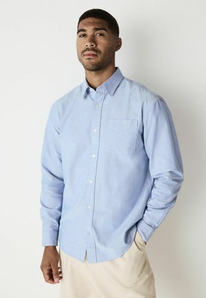 Hellblaues Button-Up-Hemd aus einer Baumwollmischung, mit langen Ärmeln, einer einzelnen Brusttasche und abgerundetem Saum. Minimales Muster, glatte Textur.
