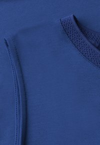 Gros plan sur un tissu tricoté bleu montrant un col en V et une manche repliée avec des coutures détaillées.