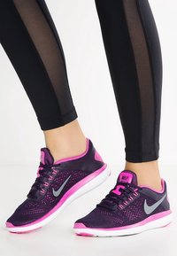 Scarpe da ginnastica viola e rosa con tomaia in mesh, accenti grigi e suola bianca, abbinate a leggins neri con pannelli laterali trasparenti.