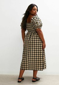 Lang, geruit jurk met een aangesloten bovenlijf, pofmouwen en een uitlopende, enkel-lange rok in zwart en beige kleuren. Knopen op de achterkant.