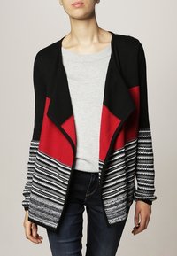 Cardigan lavorato a maglia nero e rosso con accenti grigi, caratterizzato da un motivo a righe, design aperto davanti e maniche lunghe, indossato sopra un top grigio.