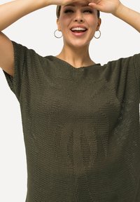 Olivengrüner gestrickter Oberteil mit lockerer Passform, kurzen Ärmeln und einer strukturierten Webart mit einem geprägten Muster auf der Vorderseite.