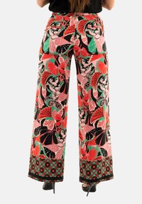 Pantalons larges avec un motif floral vibrant en rouge, rose, vert et noir, avec une bordure décorative au niveau de l'ourlet.