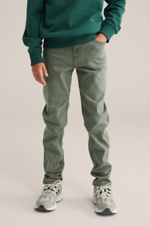 Groene katoenen jeans met een slim fit, voorzien van frontzakken en een subtiele textuur. Gecombineerd met grijze en witte sportschoenen.