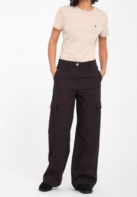 T-shirt beige a maniche corte abbinato a pantaloni cargo neri a gamba larga con tasche laterali e chiusura con bottone anteriore.