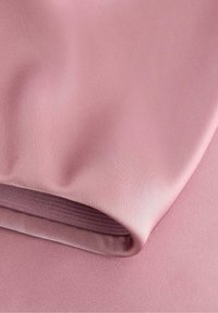 Tessuto rosa, liscio e con leggero lucido, con un bordo ripiegato e una texture a coste lungo una cucitura. Materiale leggero e flessibile.