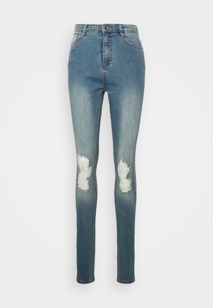 Jeans ajustados azul de talle alto con parte delantera desteñida y parches desgastados en las rodillas, con cierre delantero de botón y cremallera.