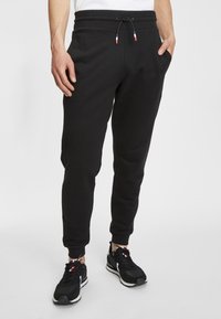 Zwarte joggingbroeken met een geribde tailleband en trekkoord, met zijzakken, tapse pijpen en een zachte textuur. Gekocht met zwarte sneakers.