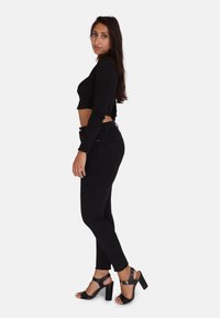 Top negro recortado de manga larga, combinado con jeans skinny negros de cintura alta y sandalias de tacón negro con tiras, mostrando un ajuste elegante.