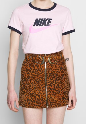 Osoba nosząca jasnoróżową koszulkę Nike z czarnymi wykończeniami oraz spódnicę w pomarańczowy wzór lamparta z wysokim stanem, z przednim zamkiem błyskawicznym i złotym paskiem z klamrą.