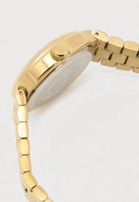 Kuldne käekell lingitud rihmaga näitab külgvaadet, sealhulgas kroon ja tagakorpus valgel taustal.