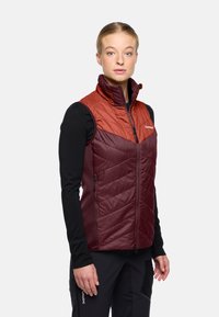 Geïsoleerde vest met een twee-kleurig ontwerp, met een oranje bovenstuk en een bordeauxrode ondersectie. Gemaakt van glanzende stof met chevron-quilting en gevoerde zakken met rits.