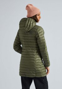 Groene gewatteerde jas met een capuchon, met een verticale gestikte ontwerp. Bevat een logo op de achterkant en wordt gecombineerd met een roze gebreide muts.