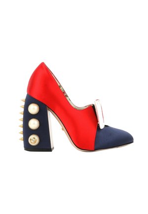 Chaussure à talons hauts rouge et marine avec pointes dorées sur le talon bloc, gros boutons en perle et nœud blanc décoratif à l'avant.