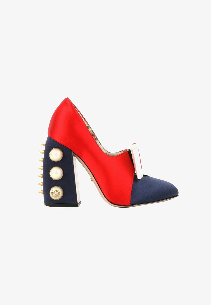 Chaussure à talons hauts rouge et marine avec pointes dorées sur le talon bloc, gros boutons en perle et nœud blanc décoratif à l'avant.