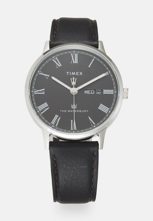 Montre à bracelet en cuir noir avec un boîtier rond en argent, un cadran gris, des chiffres romains blancs et un affichage de la date pour mercredi.