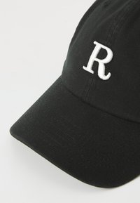 Casquette de baseball noire en coton avec une visière incurvée et une lettre "R" brodée en blanc à l'avant. Tissu texturé avec des détails de couture.
