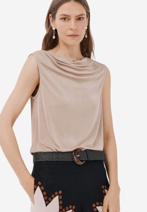 Top beige senza maniche con scollatura drappeggiata, abbinato a pantaloni scuri con un motivo floreale e una cintura intrecciata con fibbia rotonda.