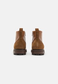 Botine din suede maro, cu un panou din piele netedă, talpă din cauciuc plat și două fermoare verticale în spate pentru un acces ușor.