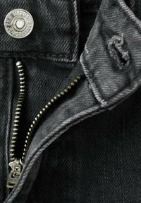 Černé džínové kalhoty s částečně rozepnutým kovovým zipem a kovovým knoflíkem s rytinou "MNG JEANS ZALOŽENO 1989."