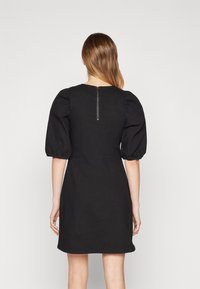 Robe noire avec des manches courtes bouffantes, taille cintrée et fermeture éclair au dos. Tissu lisse et design mi-genou sans embellissements supplémentaires.