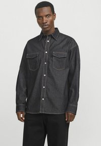 Camicia di jeans scuri con colletto, maniche lunghe, due tasche sul petto e cuciture a contrasto. Bottoni frontali e nei polsini.