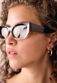 Schwarze Cateye-Sonnenbrille mit reflektierenden Gläsern und einem abgestuften braunen Rand. Verfügt über ein glänzendes Finish und ein markantes, kantiges Design.