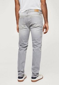 Jeans de mezclilla de color gris claro con un corte recto, que cuentan con bolsillos traseros y una etiqueta de cuero marrón en la cintura. Llevados con zapatillas blancas.