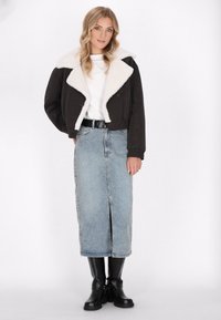 Schwarze cropped Jacke mit weißem Kunstfellkragen, weißes Hemd, hellblaue Jeansrock mit Schlitz vorne und kniehoche schwarze Stiefel.