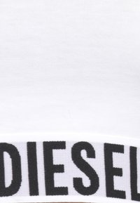 Tessuto di cotone bianco con un ampio cintura nera con la scritta "DIESEL" in caratteri bold. Texture liscia e design semplice.