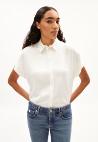 Witte blouse met korte mouwen en een knoopsluiting aan de voorkant, gladde textuur en een ontspannen pasvorm, gecombineerd met blauwe denim jeans met platte zakken.
