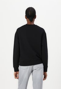 Felpa nera con colletto rotondo, polsini e orlo a costine. Design casual, vista posteriore, abbinata a jeans grigi chiari. Tessuto dalla texture liscia.