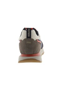 Sneaker con tomaia in pelle beige, dettagli in suede grigio e particolari arancioni; presenta una suola in gomma resistente e la scritta "1985" in rilievo sul tallone.