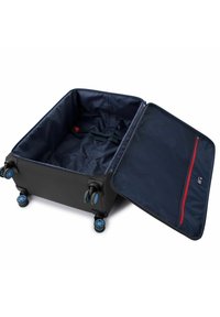 Maleta dura negra con ruedas azules. Abierta con interior en azul marino, cuenta con un bolsillo con cremallera roja y una correa de sujeción en la base.