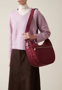 Burgunderfarbene, strukturierten Leder Hobo-Tasche mit einem goldenen Reißverschluss, ausgestattet mit einem breiten Träger, der mit "BORBONESSE" geprägt ist. Begleitet von einem lilafarbenen Pullover.