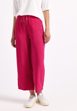 Pantalons larges roses avec un waistband à cordon de serrage, fabriqués en tissu léger. Associés à des baskets blanches pour un look décontracté.