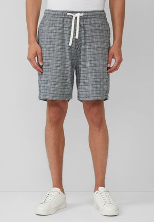 Grau-weiße gemusterte Shorts mit einem Kordelzugbund, aus leichtem Stoff und mit lockerer Passform. Kombiniert mit weißen Sneakers.