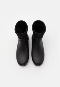 Melni gumijas potītes zābaki ar gludu apdari un mīkstu auduma oderi, ar noapaļotu purngalu un vienkāršu, minimālistisku dizainu.