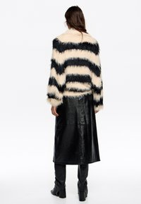 Nepbont jack met crèmekleurige en zwarte zigzagstrepen; gecombineerd met een zwarte leren maxi-rok; gladde textuur, lange mouwen.