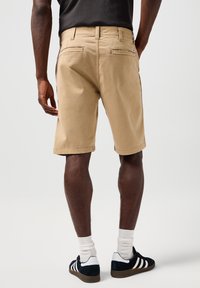 Beżowe szorty bawełniane o prostym kroju, z kieszeniami z przodu i z tyłu oraz podwiniętymi nogawkami. Noszone z czarno-białymi trampkami i skarpetkami typu crew.