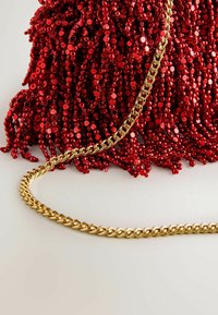 Punane helmedest käekott, millel on kaskaadne frantsi disain, koos punutud kuldse metallketiga. Peegeldavad helmestikud loovad tekstuuri.