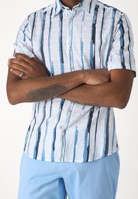 Koszula z krótkim rękawem zapinana na guziki, w jasnoniebieskim kolorze z pionowymi paskami w ciemnoniebieskim i granatowym. Materiał o fakturze, z usztywnianym kołnierzykiem i detalami z guzików.