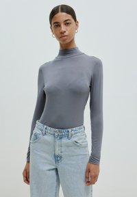 Grijze lange mouwen bodysuit met een hoge kraag, gecombineerd met lichtgewassen, high-waisted jeans. Soepele stof met een aansluitende silhoeët.